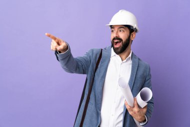 Miğferli genç mimar, elinde izole edilmiş mor arkaplanı gösteren planlar tutuyor.