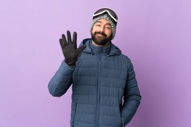 İzole edilmiş mor arka planda snowboard gözlüklü kayakçı beş parmaklı sayıyor.