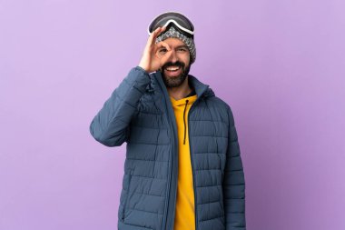 İzole edilmiş mor arka planda snowboard gözlüklü kayakçı parmaklarıyla tamam işareti gösteriyor.