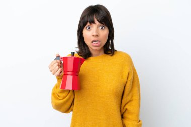 Beyaz arka planda kahve demliği tutan genç melez bir kadın. Şaşırtıcı bir yüz ifadesi var.