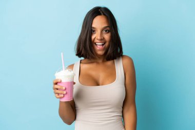 Çilekli milkshake 'i olan genç bir kadın mavi arka planda izole edilmiş ve yüzünde sürpriz bir ifade var.
