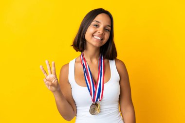Beyaz arka planda madalyalı genç Asyalı kadın mutlu ve parmaklarıyla üçe kadar sayıyor.
