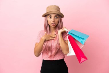 Pembe arka planda izole edilmiş alışveriş çantalı genç melez kadın sağa bakarken şaşırmış ve şok olmuştu.