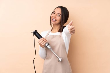 Genç esmer kız, el blendırını izole edilmiş arka planda kullanıyor. Başparmakları havada çünkü iyi bir şey oldu.