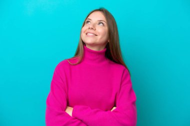 Genç Litvanyalı kadın mavi arka planda izole edilmiş gülümserken yukarı bakıyor