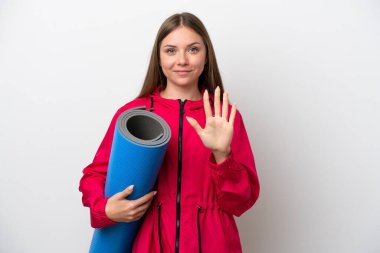 Genç bir kadın yoga derslerine giderken beyaz arka planda bir minder tutuyor.   