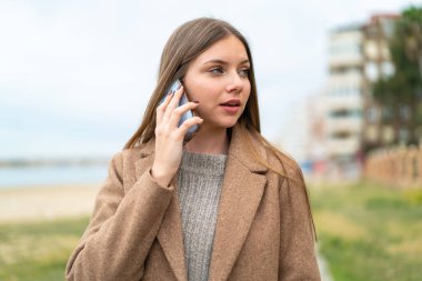 Genç, güzel, sarışın bir kadın cep telefonuyla biriyle sohbet ediyor.