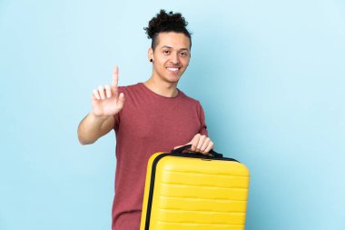 Beyaz adam izole edilmiş mavi arka planda seyahat valiziyle geziyor ve bir kişi sayıyor.