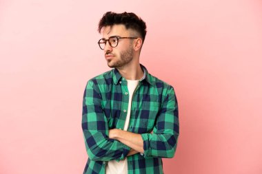 Pembe arka planda izole edilmiş genç beyaz adam kollarını kavuşturuyor.