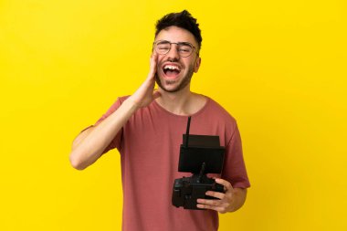 Elinde uzaktan kumanda olan bir adam sarı arka planda izole edilmiş ve ağzı açık bağırıyor.