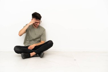 Beyaz arka planda izole bir şekilde yerde oturan genç beyaz adam gülüyor.