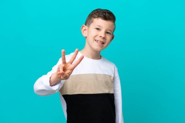 Küçük çocuk mavi arka planda tek başına mutlu ve parmaklarıyla üçe kadar sayıyor.