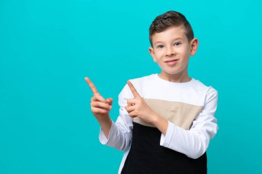 Küçük çocuk mavi arka planda izole edilmiş korkmuş ve kenarı işaret ediyor.