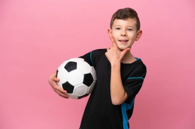 Küçük beyaz futbolcu çocuk pembe arka planda izole edilmiş mutlu ve gülümsüyor.