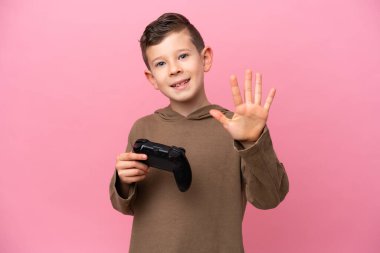 Pembe arka planda izole edilmiş bir bilgisayar oyunu kontrolörüyle oynayan beyaz çocuk parmaklarıyla beşi sayıyor.