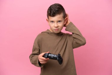Pembe arka planda izole edilmiş bir bilgisayar oyunu kontrolörüyle oynayan beyaz bir çocuk.