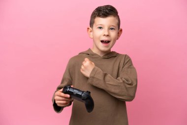 Pembe arka planda izole edilmiş bir bilgisayar oyunu kontrolörüyle oynayan beyaz bir çocuk zaferi kutluyor.