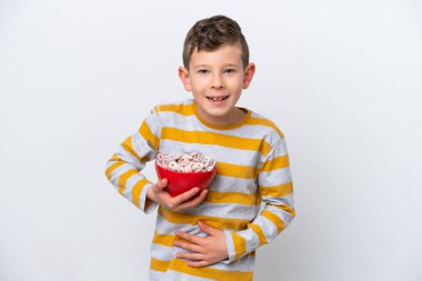 Beyaz arka planda izole edilmiş mısır gevreği kasesi tutan küçük beyaz çocuk çok gülümsüyor.