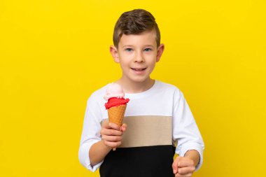 Sarı arka planda izole edilmiş kornet dondurmalı küçük beyaz çocuk galibiyetini kutluyor.