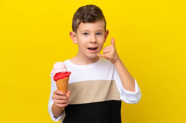 Sarı arka planda izole edilmiş kornet dondurması olan beyaz bir çocuk telefon jesti yapıyor. Bana geri dönüş işareti ver.