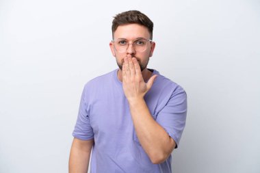 Beyaz arka planda izole edilmiş beyaz tenli genç bir adam ağızı eliyle kapatıyor.