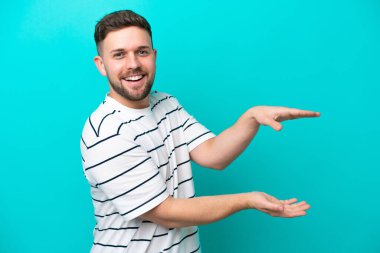 Genç beyaz adam mavi arka planda izole edilmiş bir ilan vermek için kopyalama alanı tutuyor.