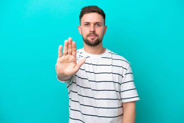 Mavi arka planda izole edilmiş genç beyaz adam dur hareketi yapıyor.