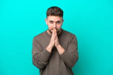 Mavi arka planda izole edilmiş genç beyaz adam avuç içlerini bir arada tutuyor. İnsan bir şey ister.