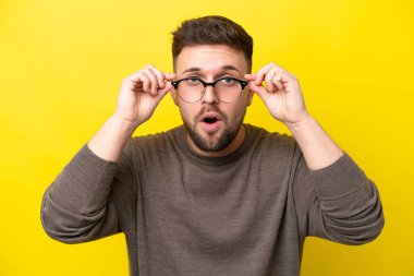 Sarı arka planda gözlüklü ve şaşkın bakışlı genç beyaz adam.