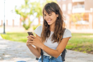 Açık havada cep telefonu kullanan genç bir kadın.