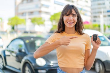 Dışarıda arabanın anahtarlarını tutan ve doğrultan genç bir kadın.