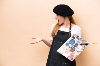 Beyaz tenli genç bir kadın bej arka planda izole edilmiş bir palet tutuyor.