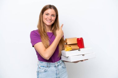 Beyaz arka planda izole edilmiş fast food tutan güzel sarışın kadın bir ürünü sunmak için yan tarafı işaret ediyor.