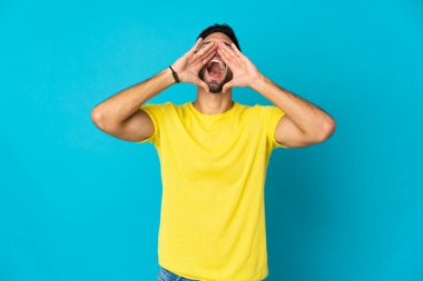 Kafkasyalı genç adam mavi arka planda izole edilmiş bağırıyor ve bir şeyler söylüyor.