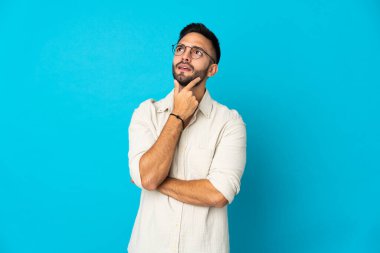 Kafkasyalı genç adam mavi arka planda izole edilmiş. Şüpheleri var.