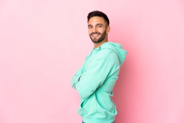 Pembe arka planda izole edilmiş, kolları bağlı ve mutlu genç beyaz bir adam.