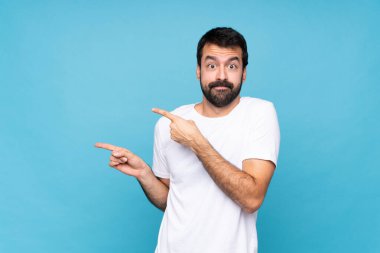 Sakallı genç adam mavi arka planda korkmuş ve kenarı işaret ediyor.