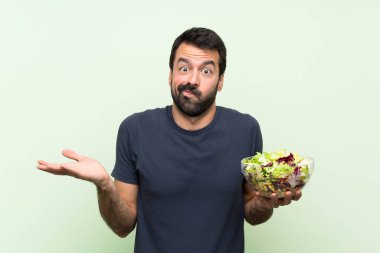 Yeşil duvarın üstünde salatalı yakışıklı genç adam bir şeyi anlamadığı için mutsuz.