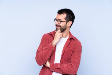 Mavi arka planda kadife ceket giyen genç beyaz adam yan tarafa bakıyor.