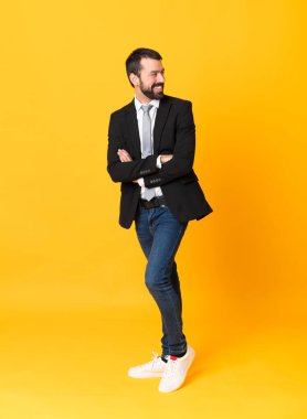Kolları bağlı ve mutlu bir şekilde izole edilmiş sarı arka plan üzerinde tam boy iş adamı fotoğrafı.