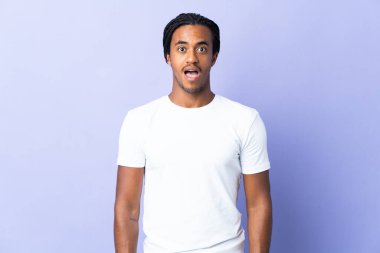 Süslü örgülü genç Afrikalı Amerikalı adam mor arka planda şaşırmış bir yüz ifadesiyle izole edilmiş.