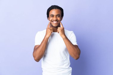 Örgülü genç Afrikalı Amerikalı adam mor arka planda izole edilmiş mutlu ve hoş bir ifadeyle gülümsüyor.