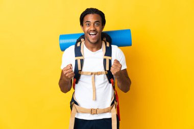 Sarı arka planda büyük bir sırt çantalı genç dağcı zaferi kutluyor.