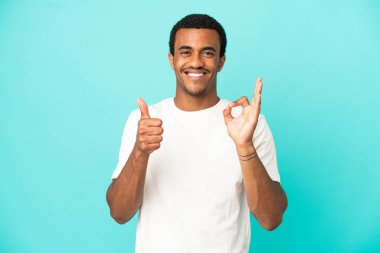 İzole edilmiş mavi arka planda Afro-Amerikalı yakışıklı bir adam işaret ve baş parmak hareketi gösteriyor.