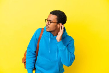 Sarı arka planda yaşayan Afrikalı Amerikalı bir öğrenci. Kulağına elini sürerek bir şey dinliyor.