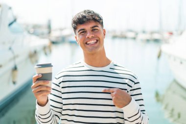 Genç İspanyol adam açık havada kahve tutuyor ve yüzünde sürpriz bir ifade var.