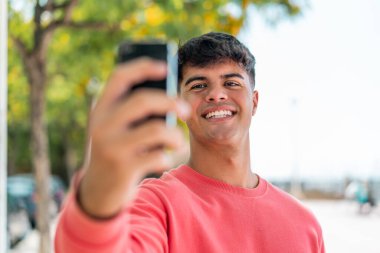 Dışarıdaki İspanyol genç adam cep telefonuyla selfie çekiyor.