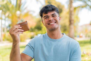 Dışardaki genç İspanyol adam mutlu bir ifadeyle cüzdanı elinde tutuyor.