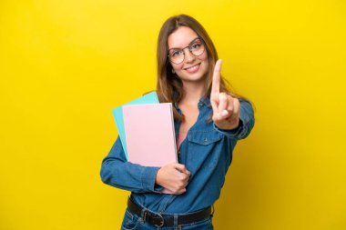 Sarı arka planda izole edilmiş genç beyaz kadın parmağını kaldırıyor ve gösteriyor.