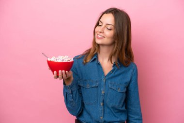 Genç, beyaz bir kadın elinde bir kase mısır gevreği tutarken mutlu bir ifadeyle pembe arka planda izole edilmiş.